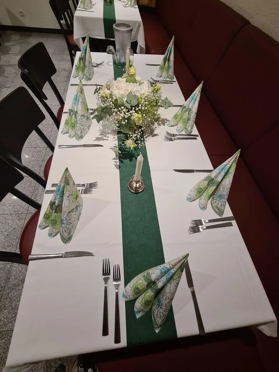 Festtafel mit grünem Tischläufer, Blumenschmuck und gefalteten Servietten